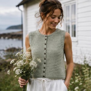 May include: A sage green sleeveless knit vest featuring a round neckline and a vertical row of small brown buttons down the centre front. The garment has a textured, ribbed stitch pattern and a straight hemline that sits at the waist.