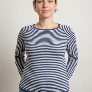 May include: A blue and white striped sweater with long sleeves. The sweater has a round neckline and a ribbed hem. The stripes are horizontal and evenly spaced. The person in the image is wearing blue jeans.