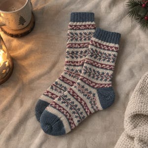 May include: A pair of knit socks featuring a fair isle pattern in shades of blue, cream, and maroon. The socks have a ribbed cuff, a reinforced heel, and a solid blue toe section. The intricate design consists of repeating geometric and floral motifs.