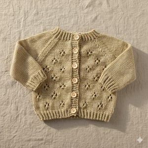 Peut inclure: Un cardigan de bébé beige clair avec une fermeture boutonnée. Le pull tricoté présente un motif ajouré délicat et des poignets côtelés. Le cardigan est fait d'un fil doux et texturé et a une encolure ronde. Les boutons sont de couleur beige clair.
