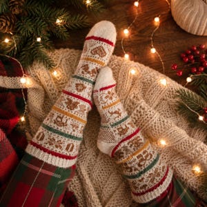Può includere: Un paio di calze in maglia color crema con un motivo festivo di cuori, renne e fiocchi di neve marroni, accentuato da strisce orizzontali rosse, gialle e verdi. Le calze sono indossate sopra un tessuto a quadri rosso e verde.