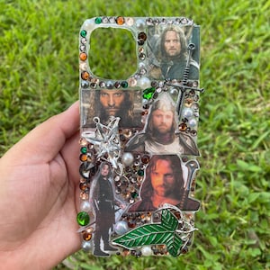 May include: A clear phone case decorated with images of a character from The Lord of the Rings. The case is embellished with various rhinestones, pearls, and green and orange gems. A silver star and a green leaf design are also included.