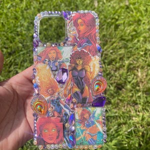 Könnte beinhalten: Ein Handyhülle mit Comic-Illustrationen in Rot, Lila und Blau. Die Hülle ist mit einem Rand aus kleinen Kristallen und größeren dekorativen Edelsteinen verziert.