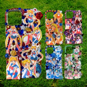 Puede incluir: Varias fundas de teléfono decoradas con personajes de anime de Sailor Moon. Las fundas presentan varios diseños con pedrería de colores, perlas y recortes de personajes. Las fundas están sobre un fondo de hierba verde.