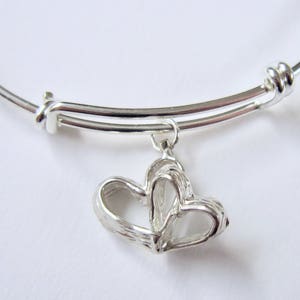 May include: A silver expandable bangle bracelet with a charm of two intertwined hearts.