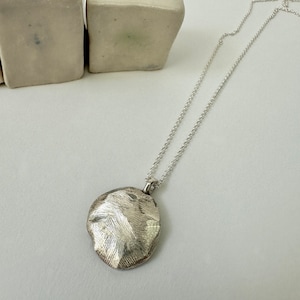 May include: A silver necklace with a textured round pendant. The pendant has a hammered finish and a slightly irregular shape.