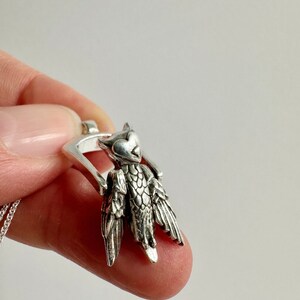 Puede incluir: Collar con colgante de plata en forma de búho con alas detalladas y cabeza en forma de corazón. El colgante está unido a una cadena de plata.