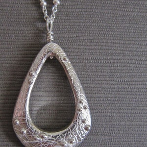 May include: A silver teardrop-shaped pendant necklace with a textured surface and small silver beads around the edge.