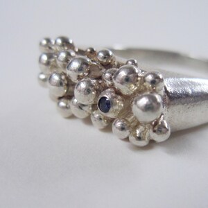 May include: A silver ring with a cluster of small, round beads and a single blue gemstone in the center.