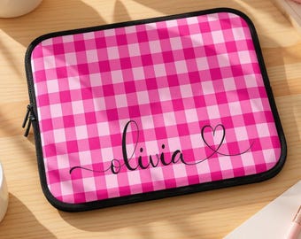 May include: A pink and white gingham pattern laptop sleeve with a black zipper and trim. The name "Olivia" is written in cursive script with a heart symbol.