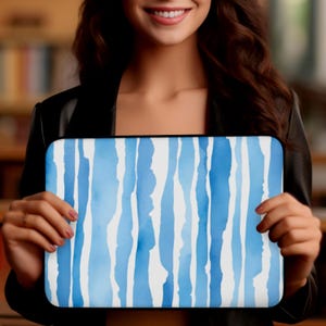May include: A rectangular laptop sleeve featuring a watercolor design of vertical blue stripes against a white background. The sleeve is held up by a person. The design has varying shades of blue, creating a flowing, artistic pattern.