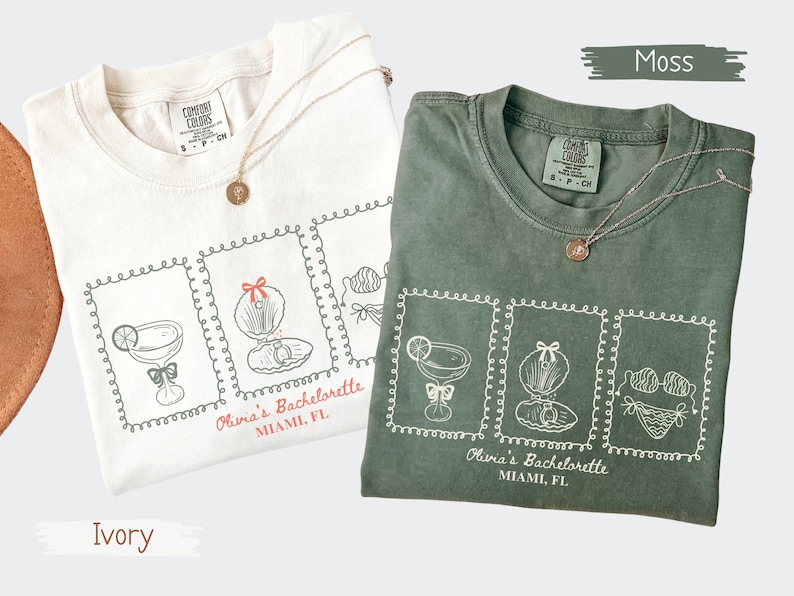 May include: Two t-shirts, one ivory and one moss green, are displayed. Each shirt features a graphic of cocktail glasses, seashells, and lingerie, with the text "Olivia's Bachelorette, Miami, FL." Gold necklaces with round pendants are draped on the shirts.
