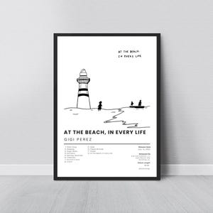 May include: A framed art print with a minimalist design. It features a lighthouse, figures, and a boat on the water. The text "AT THE BEACH, IN EVERY LIFE" is displayed above and below the illustration. The artist's name is Gigi Perez.