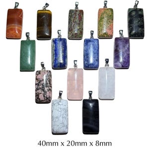 Puede incluir: Una colección de colgantes rectangulares de piedras preciosas en varios colores y patrones. Cada colgante mide aproximadamente 4 cm de largo, 2 cm de ancho y 0,8 cm de grosor. Los colgantes tienen argollas plateadas.