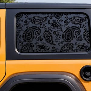 May include: Close-up of a yellow Jeep with a black window featuring a black paisley pattern. The vehicle's rear window is decorated with the intricate design. The Jeep's black trim and accents contrast with the yellow body.