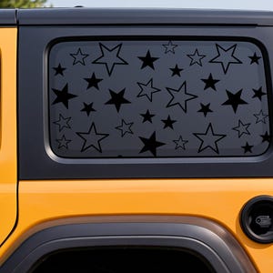 May include: A yellow SUV with a black top and window. The rear window features a pattern of black stars of varying sizes. The vehicle has a black bumper and a spare tire mounted on the back.