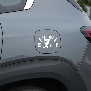 May include: White vinyl decal depicting a fuel gauge with a stick figure struggling to push the needle to the full mark. The gauge is on a gray car panel, with the letters "E" and "F" indicating empty and full.