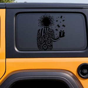 May include: Black vinyl decal of a character with curly hair, holding a gift box, and surrounded by flying insects. The decal is applied to the rear window of a yellow Jeep.