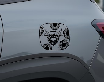 May include: A black and white decal featuring a Highland cow head surrounded by sunflowers. The decal is applied to a gray vehicle, showcasing a unique design. The image highlights the contrast between the black design and the gray background.