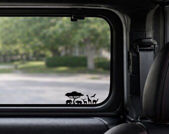 May include: Black silhouette decal featuring African wildlife, including an elephant, rhino, giraffe, and camel, under a tree. The decal is applied to a vehicle window, with a blurred outdoor background.