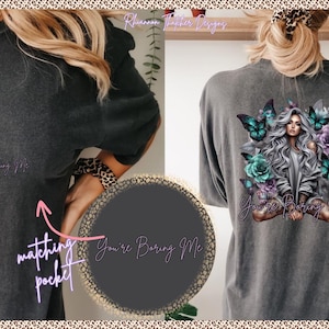 May include: Dark gray t-shirt with a matching pocket. The back of the shirt features a graphic of a woman with butterflies and flowers, with the text "You're Boring Me". The shirt is a comfortable, casual style.