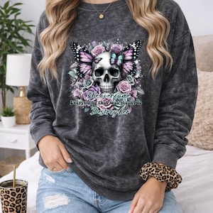 May include: Dark gray sweatshirt featuring a skull design with butterfly wings and floral accents in pink, purple, and blue. The text "She overcame Everything that was meant to Destroy her" is printed below the skull.