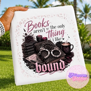 May include: A white fabric item featuring a graphic print with the text "Books aren't the only thing I like" and "bound". The design includes a stack of books, metal handcuffs, a black mug with a heart, candles, and a rose in shades of pink and black.