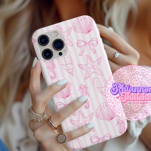 May include: A white and pink phone case featuring a pattern of seashells, starfish, seahorses, and bows. The design is set against a striped background. The case has a camera cutout and is held by a person.