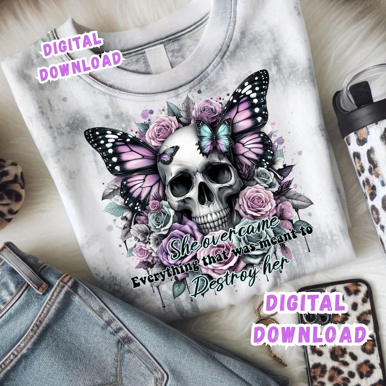 May include: White graphic t-shirt featuring a skull with butterfly wings and floral accents in shades of purple, pink, and blue. The text "She overcame everything that was meant to destroy her" is also visible.