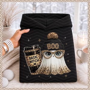 May include: A black hoodie featuring a graphic of a white ghost wearing a black beanie with the word BOO and leopard print glasses. The ghost holds a black coffee cup with a leopard print sleeve that says BASIC WITCH with a small heart.
