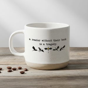 May include: A white ceramic mug with a black handle and the text "But First, Coffee" in a bold, black font. The mug is set against a neutral background, highlighting its simple design.