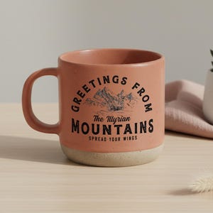 May include: A white ceramic mug with a black handle and the text "But First, Coffee" in a bold, black font. The mug is set against a blurred background. The mug appears to be approximately 10 cm tall.