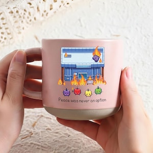 Könnte beinhalten: Ein Set aus drei Keramikbechern mit gesprenkelter, matter Oberfläche. Jeder Becher hat eine andere Farbe: Hellblau, Creme und Grau. Die Becher haben ein schlichtes, modernes Design mit runder Form und Henkel.