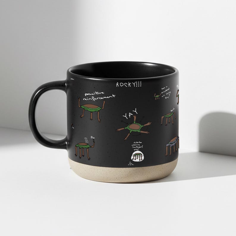 May include: A white ceramic mug with a black handle and the text "But First, Coffee" in a black, handwritten-style font. The mug is on a white surface.