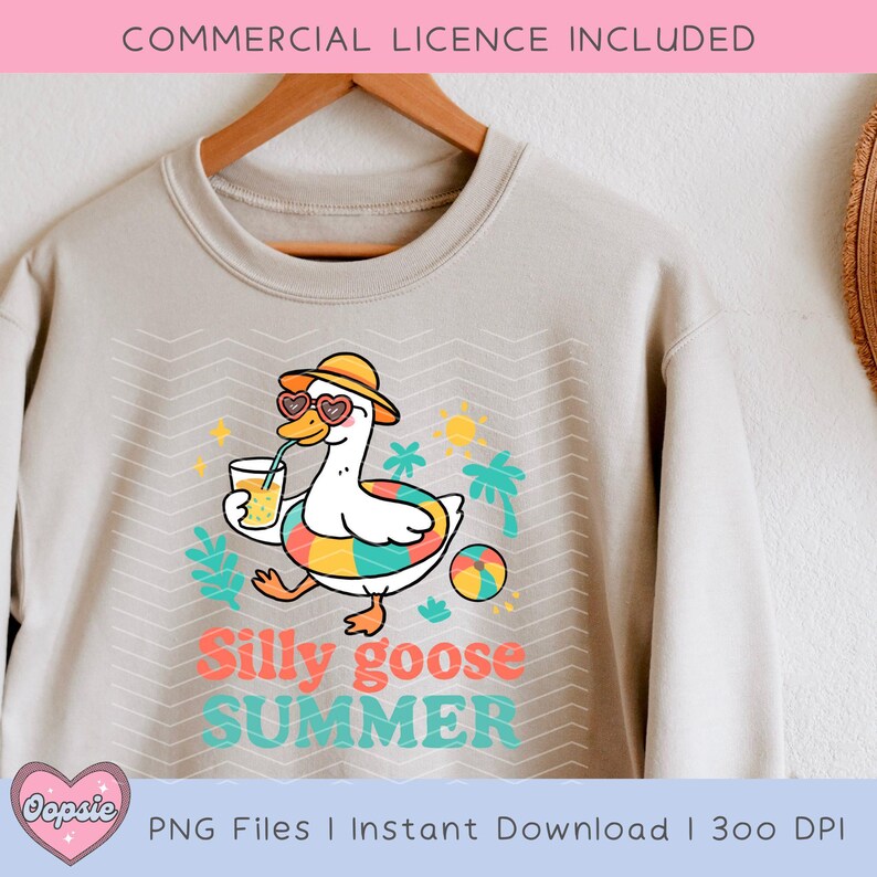 K&ouml;nnte beinhalten: Ein hellbeiger Pullover mit einem Grafikdesign eines Cartoon-G&auml;nses, der eine Sonnenbrille und einen Hut tr&auml;gt, ein Glas Saft h&auml;lt und auf einem bunten Schwimmring schwimmt. Der Text "Silly goose SUMMER" ist unter dem Gans gedruckt.
