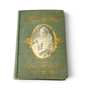 May include: A vintage book titled "Life and Reign of Queen Victoria" with gold lettering on a green cover. The cover features an oval portrait of Queen Victoria and includes the lives of King Edward VII and Queen Alexandra.