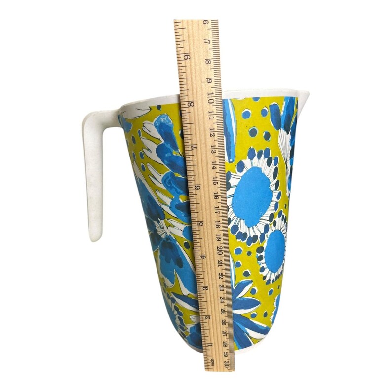 Op de afbeelding: Een vintage kan met een witte handgreep en een levendig bloemenpatroon in blauw en wit op een gele achtergrond. De kan is ongeveer 25 cm hoog, gemeten met een liniaal.