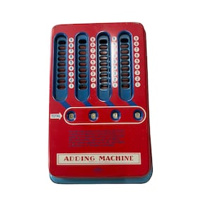 May include: A vintage red and blue metal adding machine featuring four vertical slots with numbered scales from one to nine. The device includes a horizontal display window showing the total as 0099 and the text ADDING MACHINE printed below.