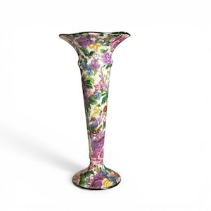 May include: A tall, floral-patterned vase with a flared top and a round base. The vase features a cream-colored background with a colorful array of flowers in shades of purple, pink, blue, and yellow. The rim and base are outlined in black.