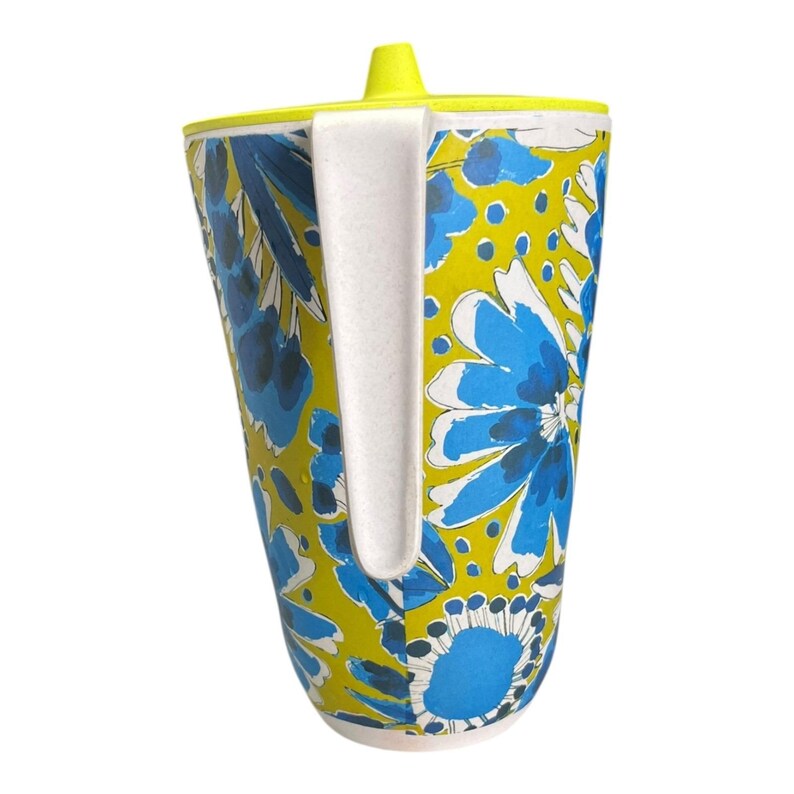 Op de afbeelding: Een hoge beker met een bloemenpatroon en een witte handgreep. Het ontwerp toont blauwe bloemen op een gele achtergrond. De rand en het deksel zijn geel en de handgreep is wit. Een decoratief item.