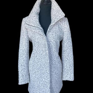 May include: A light gray textured coat with a high collar and a zipper closure. The coat is displayed on a black mannequin and has long sleeves. The fabric appears to be a soft, woven material.