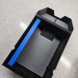 May include: A black plastic storage box with a blue divider inside. The box has a textured surface and a rectangular shape.