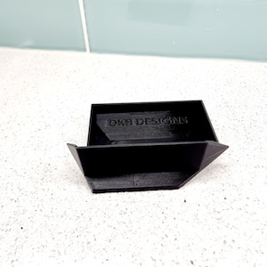 May include: A black, angular, open box with the text "DKB DESIGNS" printed on the inside.