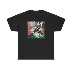 May include: Black t-shirt featuring a graphic from The Clash's album "London Calling." The design includes a black and white image of a man smashing a guitar, with the words "London Calling" in pink and green.