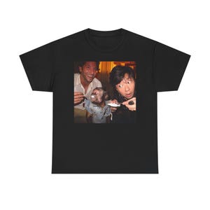 May include: Black t-shirt featuring a humorous image of two men and a monkey. The image shows the men feeding the monkey. The t-shirt is made of a soft, comfortable material.