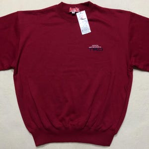 May include: A maroon crew neck sweatshirt with the text "TOYOTA MOTOR SPORTS TRD" in black. The sweatshirt has a tag attached near the collar. The fabric appears to be a soft, comfortable material.
