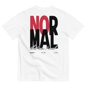 May include: White t-shirt with the word "NORMAL" in large, bold, black and red letters. Below the word "NORMAL" is the phrase "that ain't real" in a stylized font. The shirt also features a barcode and recycling symbols.