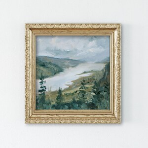 May include: A framed painting of a landscape with a river winding through a valley. The painting is in a gold frame with a decorative border. The colors are muted and the scene is peaceful.