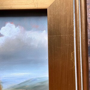 May include: A close-up of the edge of a gold-colored picture frame with a white inner border. The frame is made of wood and has a textured surface.