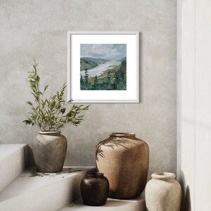 May include: A framed watercolor painting of a river winding through a green valley with trees on the banks. The painting is hanging on a light gray wall with two brown ceramic vases and a smaller black vase on a white shelf below.